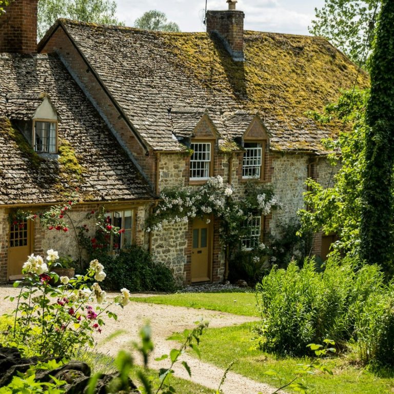 Quaint stone cottage surrounded by lush greenery and flowering plants.