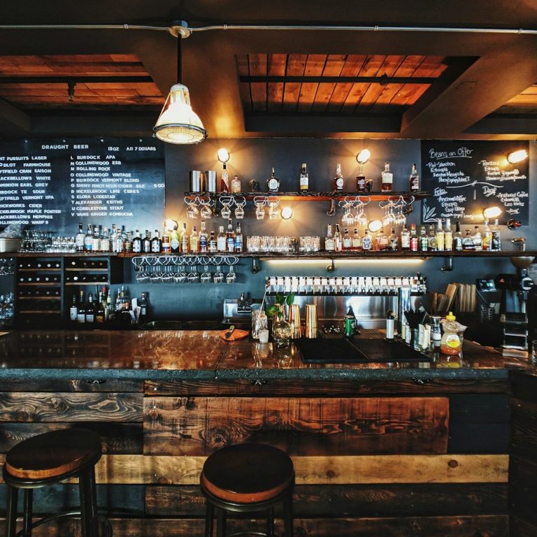 A stylish bar with wooden counters, shelves lined with bottles, and warm lighting.