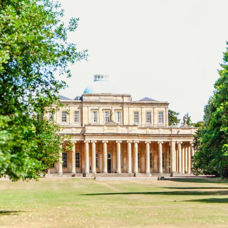 Historic building with columns surrounded by trees and landscaped grounds.