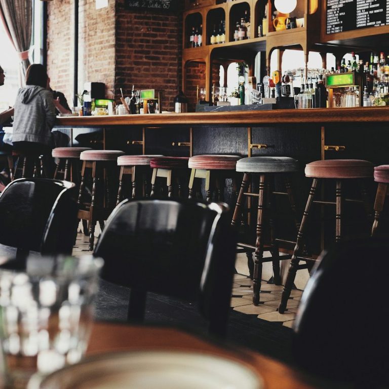 A cozy bar interior with stools, a counter, and tables set for dining.