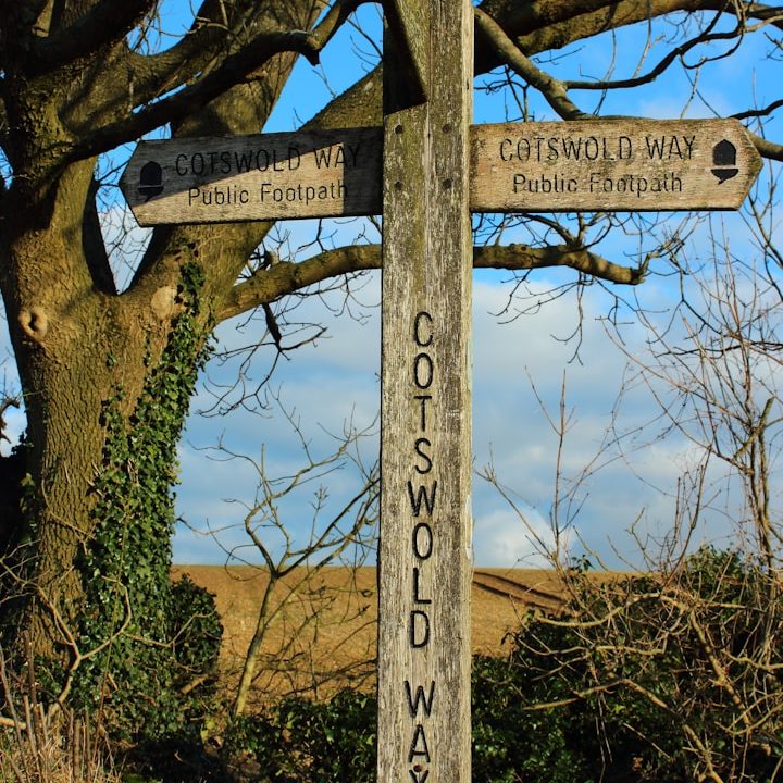 Wooden directional signpost with routes for "Cotswold Way" and nearby villages.